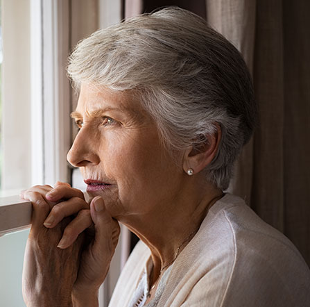 Photo of an elderly white woman looking out of a window. She seems to be in deep thought